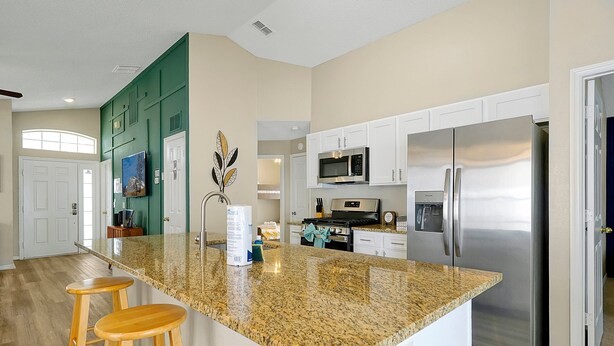 A kitchen with a granite island, wooden stools, a stainless steel refrigerator, and white cabinetry. - Family & Pet-Friendly Pool Home | Near Disney (Davenport)
