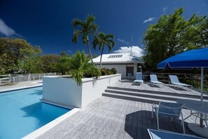 A swimming pool with a wooden deck, lounge chairs, and a covered area with umbrellas.