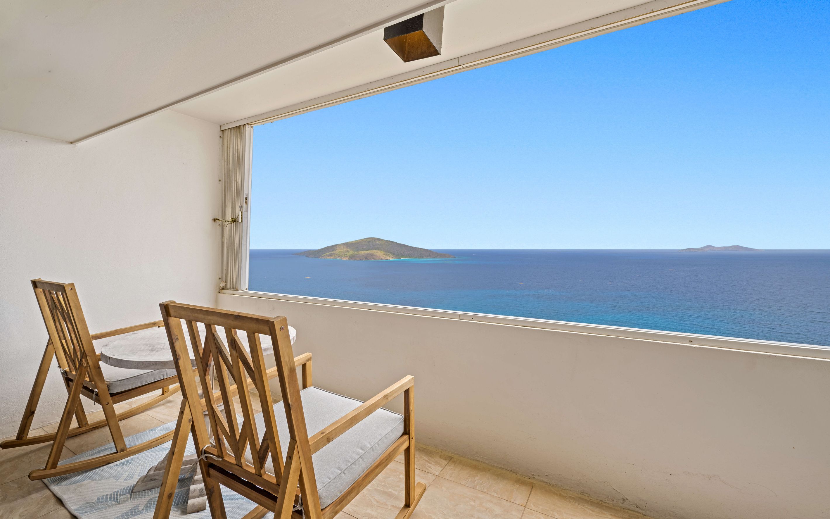 Ein Balkon mit zwei Holzstühlen und Blick auf das Meer sowie eine entfernte Insel.