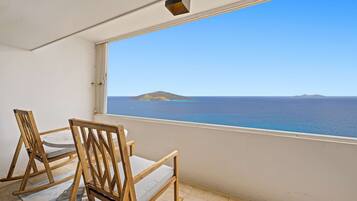 Ein Balkon mit zwei Holzstühlen und Blick auf das Meer sowie eine entfernte Insel.