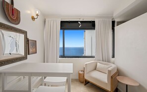 Een kamer met een witte tafel, een bank en een raam met uitzicht op zee.