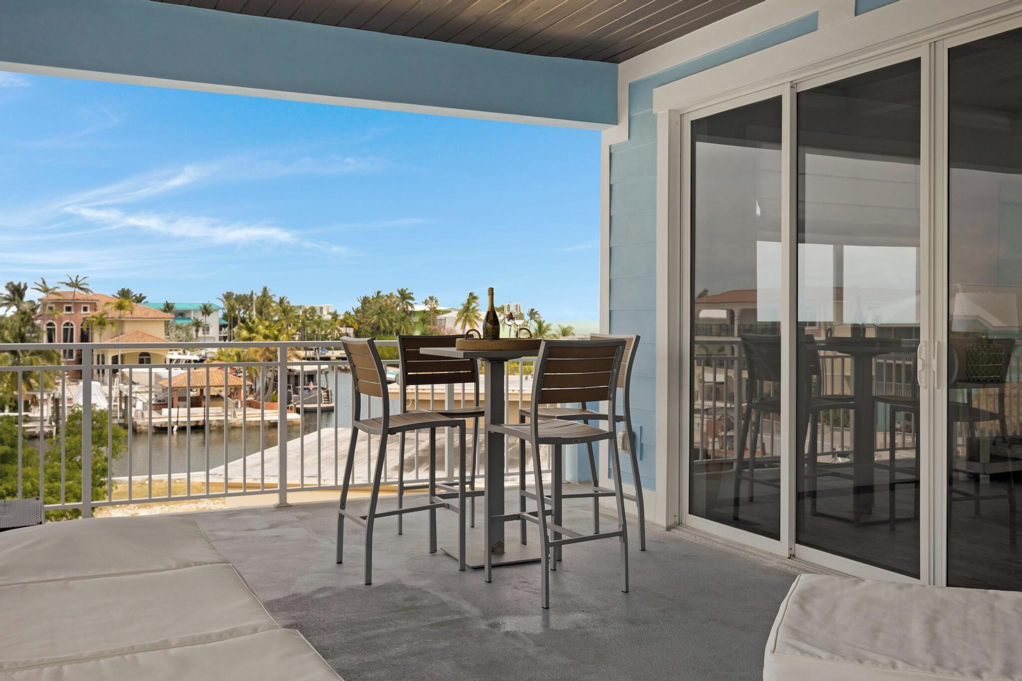 A balcony with a table and chairs, a bottle of champagne, and a view of a body of water and buildings in the background.