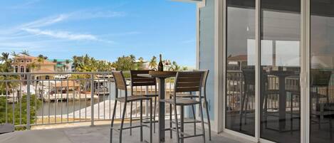 A balcony with a table and chairs, a bottle of champagne, and a view of a body of water and buildings in the background.