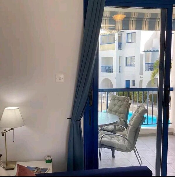 A balcony with a pool, white walls, and a blue curtain. - Paphos Holiday Apartments Pool View Apartment (Paphos)