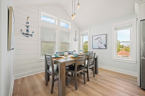 A dining area with a wooden table, chairs, and a view of the outdoors through the windows. - Sandy Pelican: Pool, Hot Tub, Elevator, Close to Beach (Corolla)