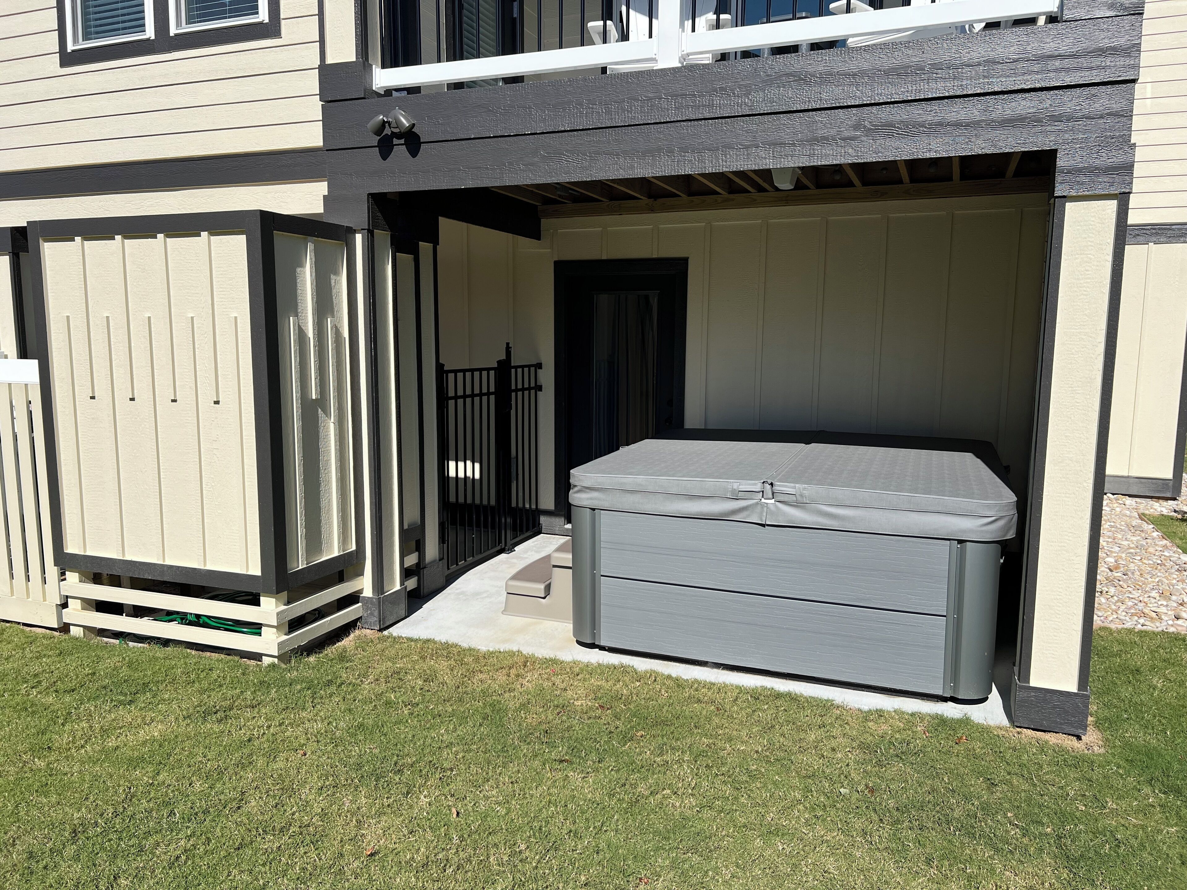 Ein überdachter Patio-Bereich mit Whirlpool, Holzlattenzaun und einer Tür zu einer Garage.