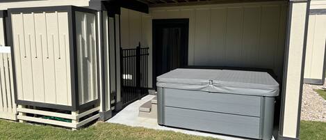 Ein überdachter Patio-Bereich mit Whirlpool, Holzlattenzaun und einer Tür zu einer Garage.