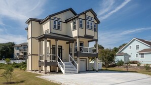 A two-story house with a covered porch and a staircase leading to the upper level. - Sandy Pelican: Pool, Hot Tub, Elevator, Close to Beach (Corolla)