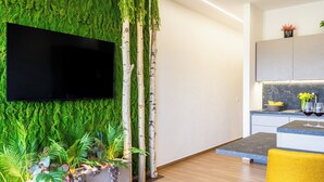 Un espacio moderno para vivir con un muro cubierto de musgo verde, un televisor de pantalla plana, una zona de cocina con encimeras de mármol y una silla amarilla.