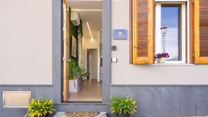 Entrada de un hotel con puerta de madera, placa con número y plantas en macetas.