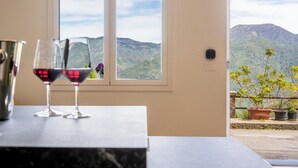 Una habitación con vistas a montañas a través de una ventana, una mesa con dos copas de vino y una planta en maceta en el balcón.