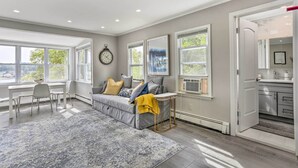 Ein modernes Wohnzimmer mit grauem Sofa, einem kleinen Tisch und einem großen Fenster.
