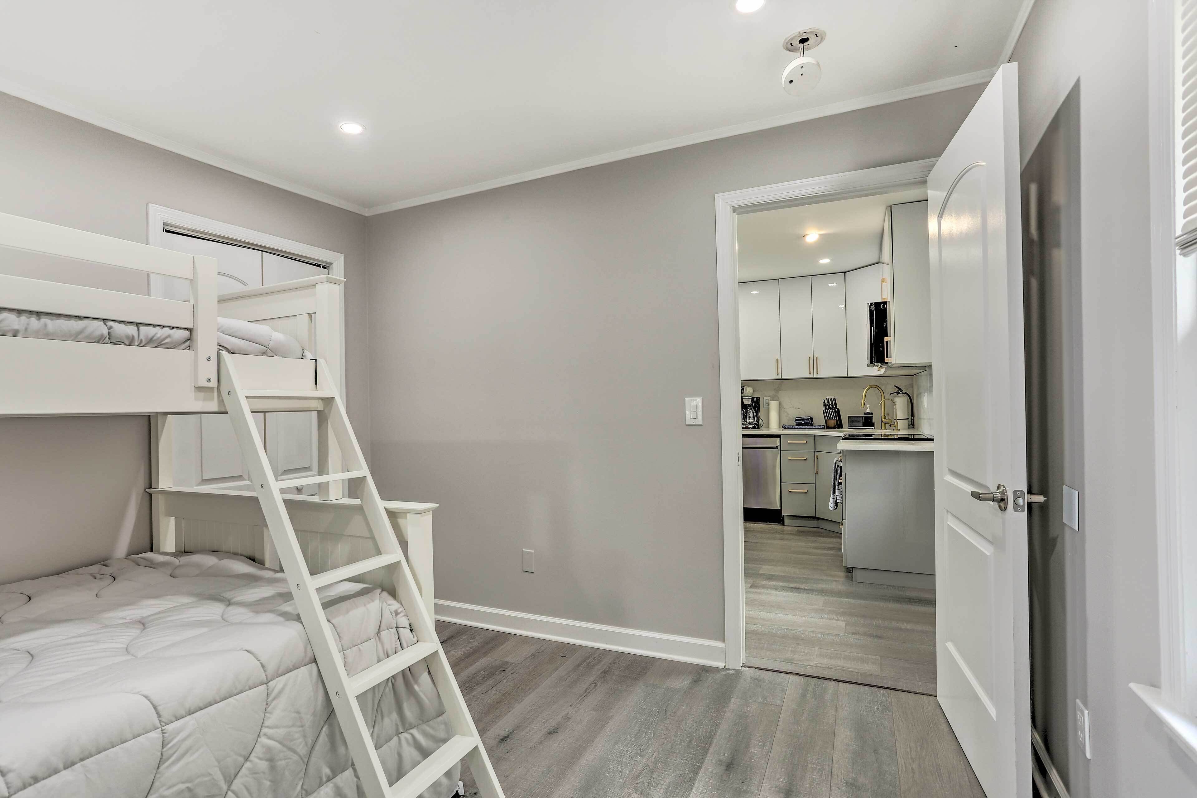 Un dormitorio con una cama litera, una escalera y una kitchenette al fondo.