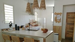 A modern kitchen with a central island, bar stools, a refrigerator, and hanging light fixtures. - Villa Lola in the heart of Baie Orientale, 100m from the beach. 800l tank (Saint martin)