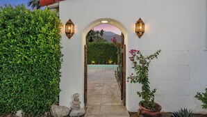 An arched entrance with a pathway leading to a pool, surrounded by greenery and a potted plant. - Casa Gitana: Moroccan-Infused Spanish Retreat with Pool and Casita (Palm Springs)