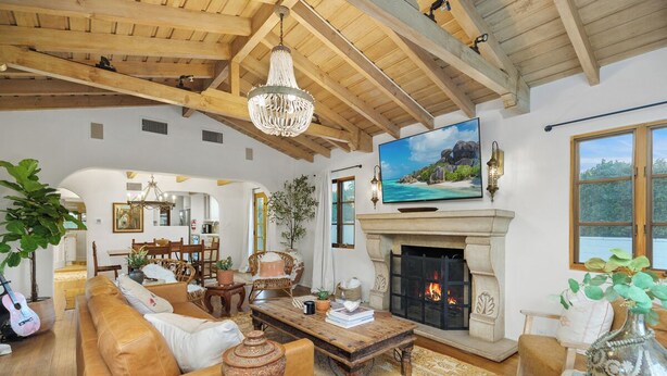 A spacious living room with a fireplace, wooden beams, a large TV, and comfortable seating. - Casa Gitana: Moroccan-Infused Spanish Retreat with Pool and Casita (Palm Springs)