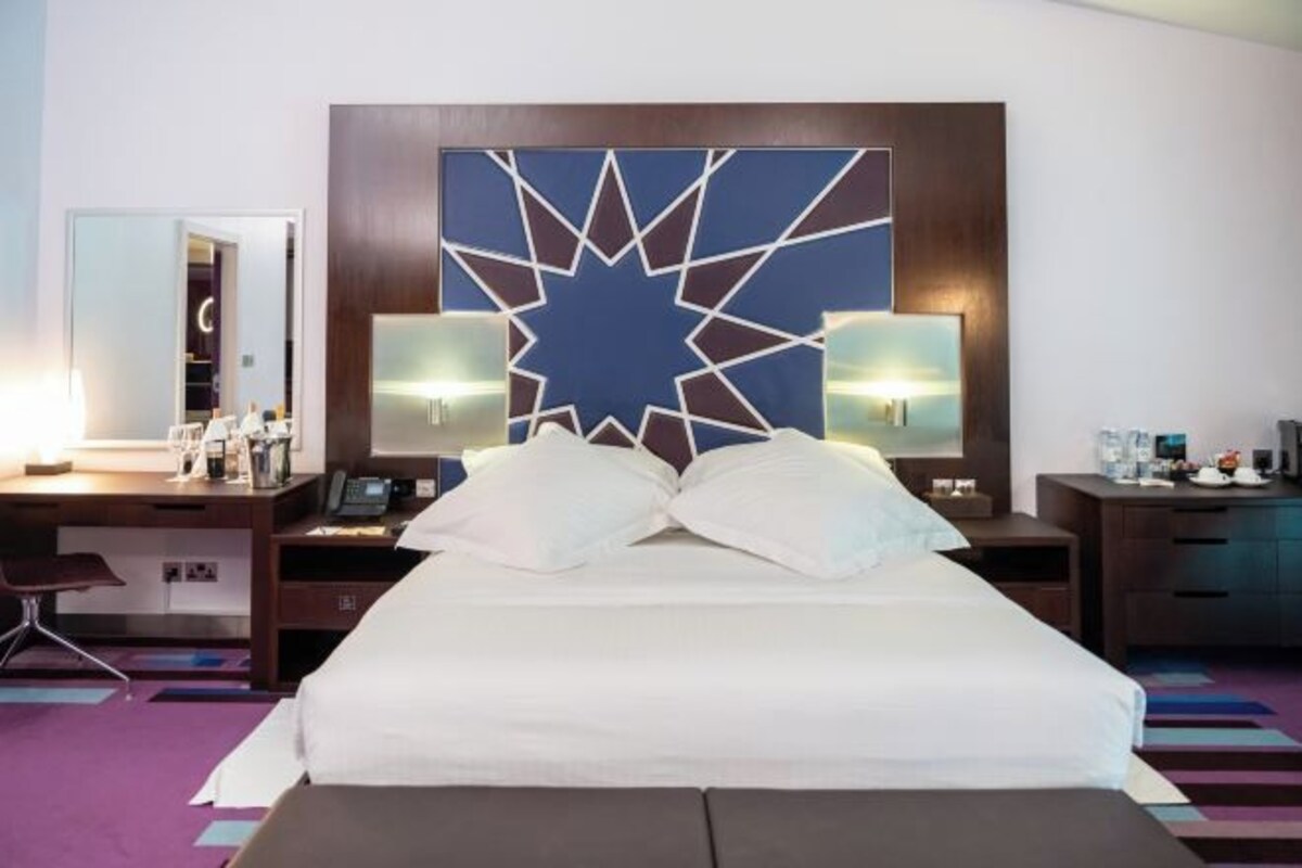 Habitació d'hotel amb un llit gran, dues taules de nit, un escriptori, una cadira i un element decoratiu a la paret.