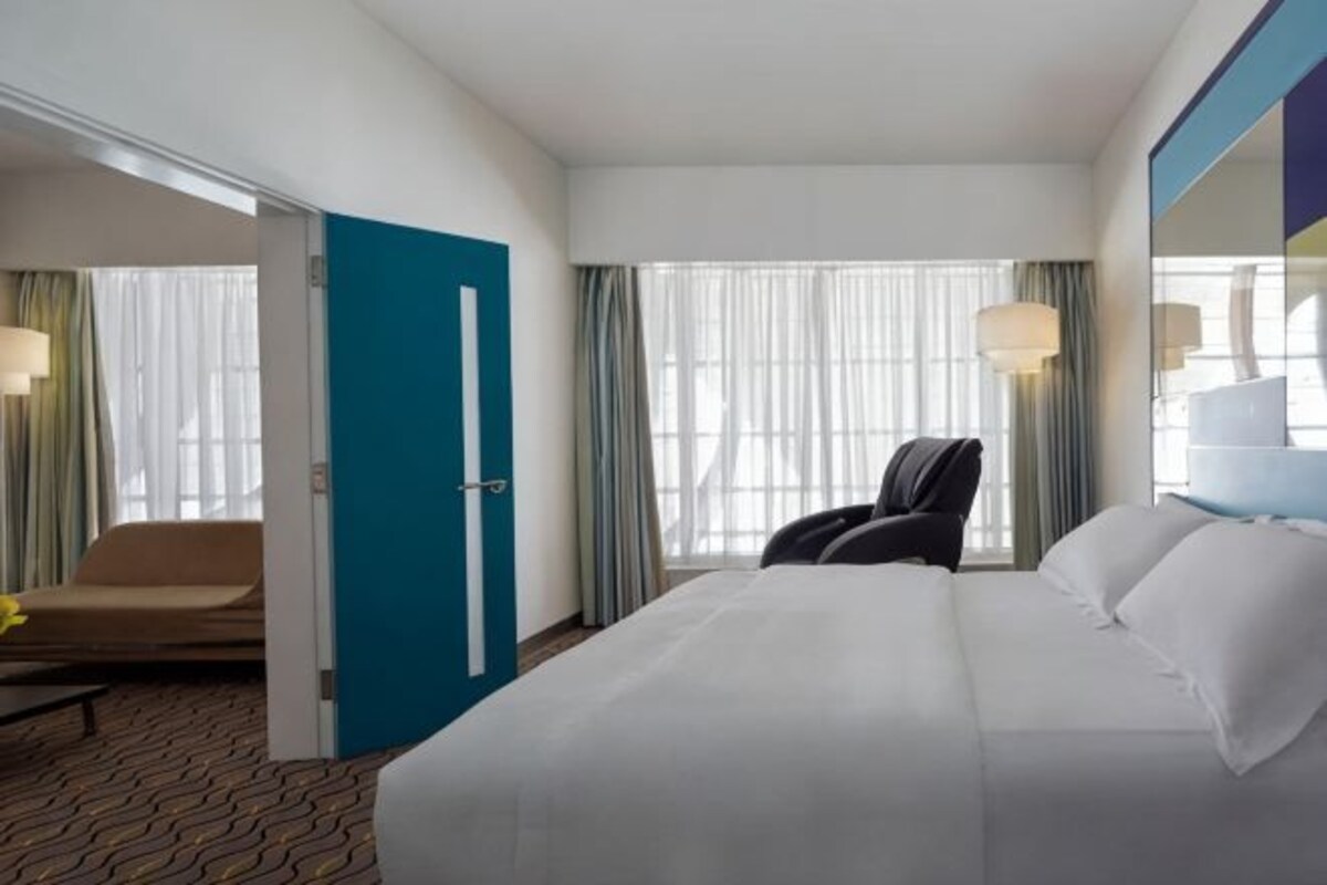 Una habitació d'hotel amb un llit gran, una cadira, un escriptori i una finestra amb cortines.