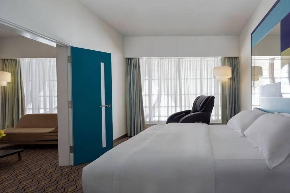 A hotel room with a large bed, a chair, a desk, and a window with curtains.