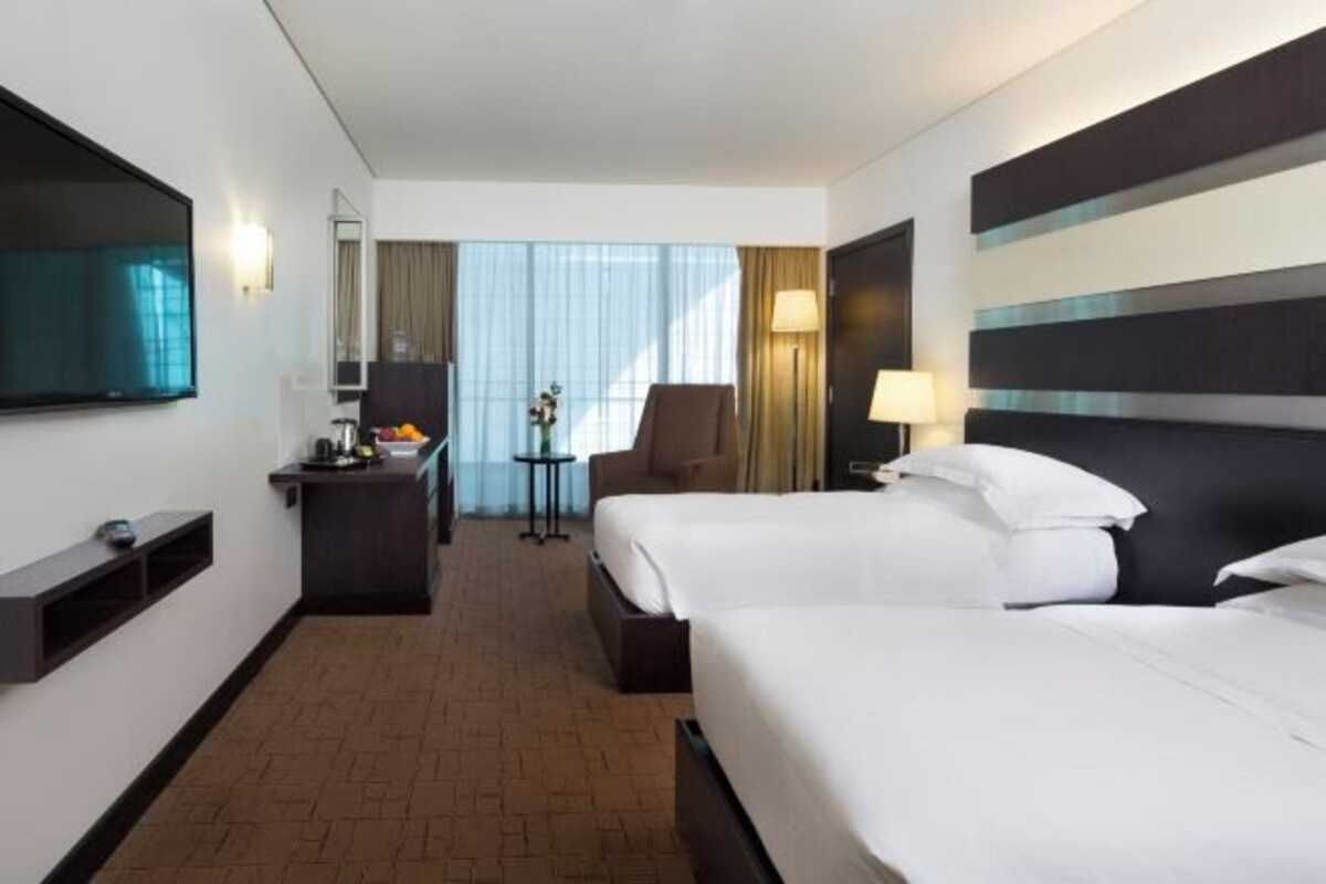 Habitación de hotel con dos camas, un escritorio, una silla, un televisor y una ventana con cortinas.