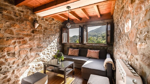 Una habitación rústica con paredes de piedra, techo de madera, un sofá, una mesa y un radiador.