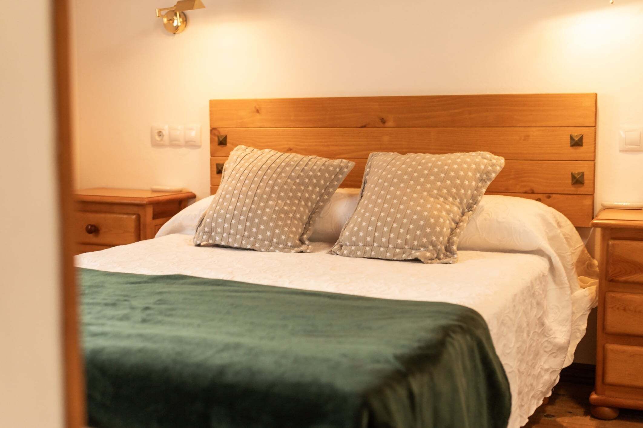 A bed with a wooden headboard, two pillows with a star pattern, a green blanket, and wooden nightstands.