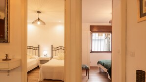 Habitación de hotel con dos camas, una mesita de noche con lámpara, una ventana con persianas y suelo de madera.