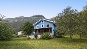 Una casa de dos pisos con fachada azul, rodeada por un césped cuidado y árboles.