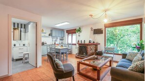 Una sala de estar con un sofá, una mesa de centro y una chimenea. Hay una zona de cocina con armarios y una mesa de comedor.