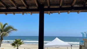 A beach view with a wooden pergola, a white tent, and palm trees.