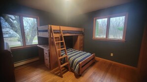 Une chambre avec un lit superposé, une échelle, un plancher en bois et deux fenêtres donnant sur des arbres.