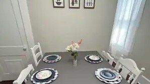A dining room with a gray tablecloth, white chairs, and a vase of flowers.
