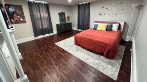 A bedroom with a large bed, dark wooden flooring, a grey rug, a dresser, and a wall with butterfly decals.