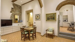 A dining area with a table and chairs, a television, and a kitchen in the background. - Lietta Apartment in Florence (Firenze)
