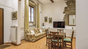 A cozy living room with a sofa, dining table, chairs, a TV, and a stone wall. - Lietta Apartment in Florence (Firenze)