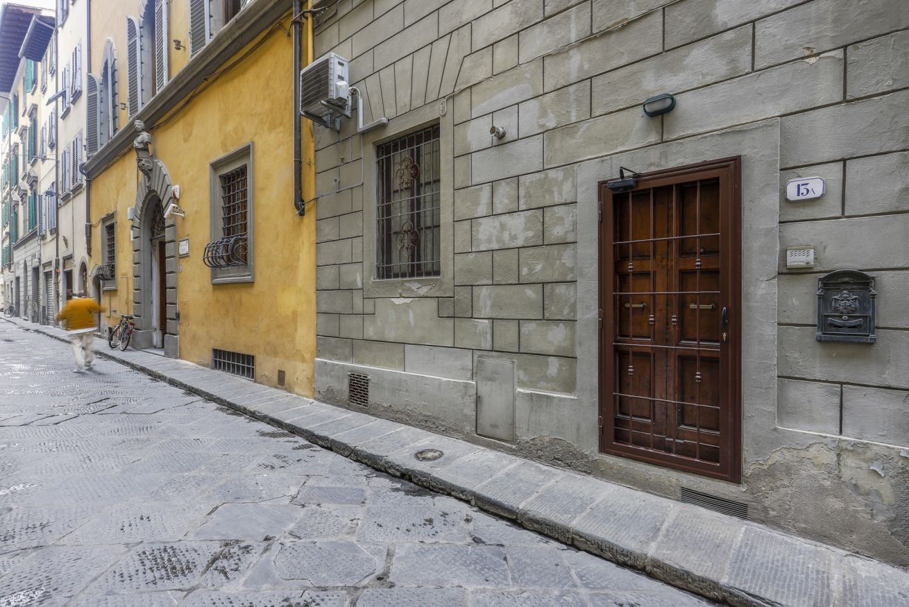 A narrow cobblestone street lined with historic buildings, featuring a yellow building with a statue and a brown door on a stone building.