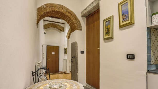 A hallway with a round mosaic table, a brick archway, and wooden doors. - Lietta Apartment in Florence (Firenze)