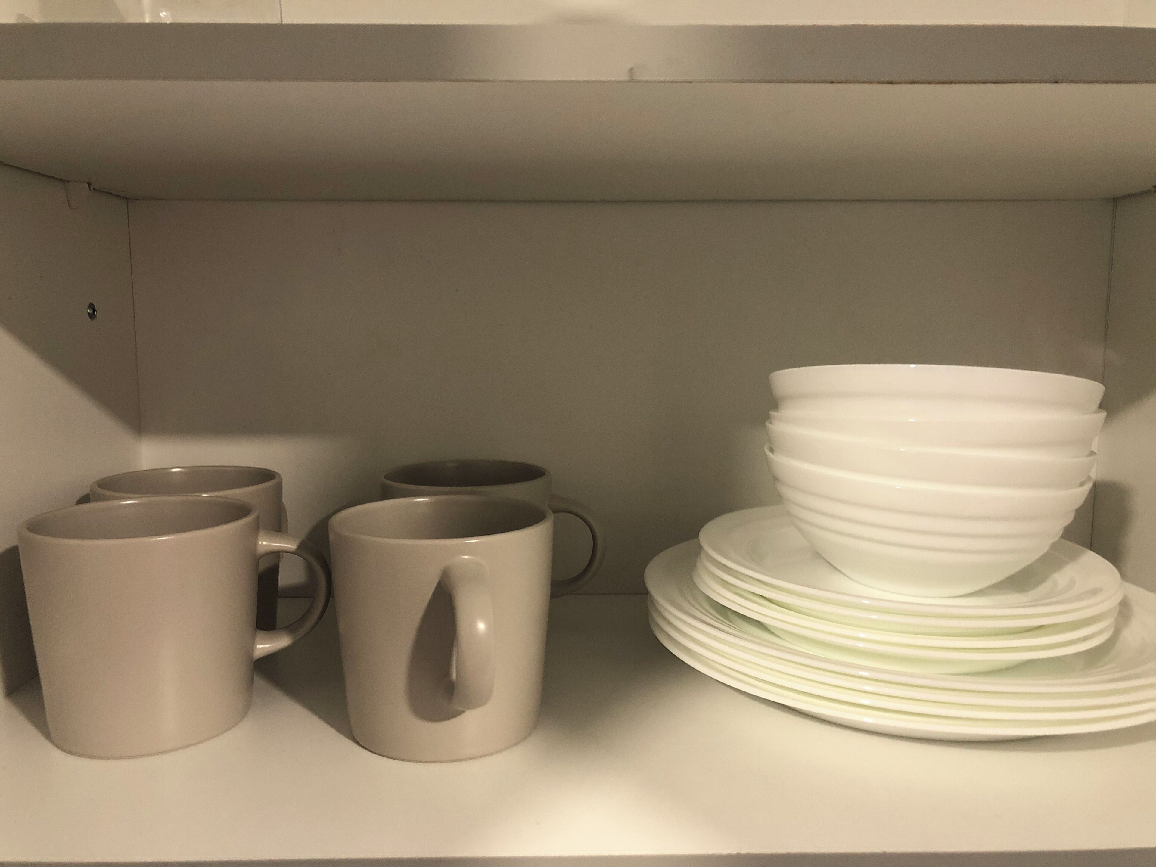 Une étagère avec des tasses blanches et des assiettes blanches empilées.