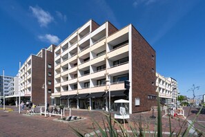 A multi-story building with a brick facade, multiple balconies, and a ground-level entrance with a glass storefront. - Strandstraße - Cozy, central 1-room apartment, close to the beach, balcony, (Westerland)