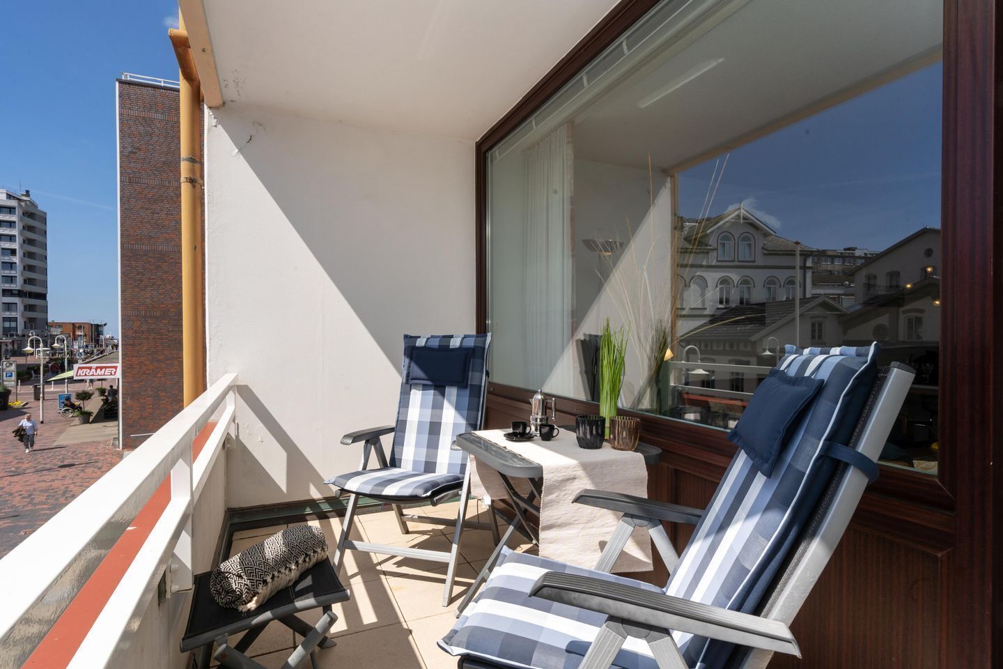 Een balkon met twee gestreepte lounge stoelen, een klein tafeltje met kop en schotel, en uitzicht op een gebouw met gebogen ramen.
