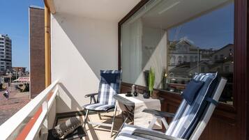 Een balkon met twee gestreepte lounge stoelen, een klein tafeltje met kop en schotel, en uitzicht op een gebouw met gebogen ramen.