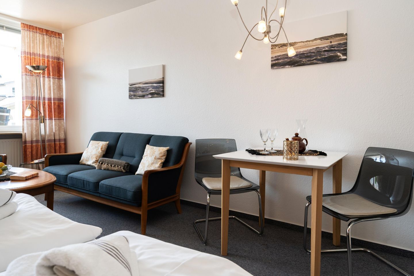 Een hotelkamer met een bank, twee stoelen, een kleine tafel met een theepot en glazen, een schilderij aan de muur en een raam met gordijnen.