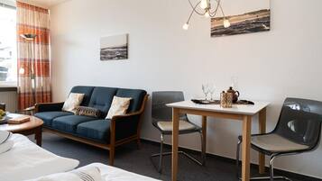 Een hotelkamer met een bank, twee stoelen, een kleine tafel met een theepot en glazen, een schilderij aan de muur en een raam met gordijnen.