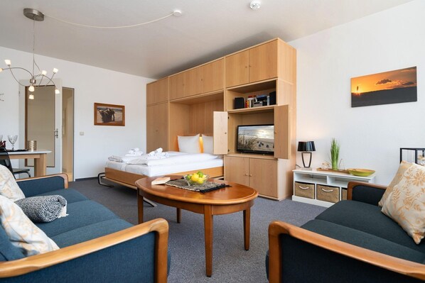 A modern hotel room with a bed, seating area, TV, and a dining table.