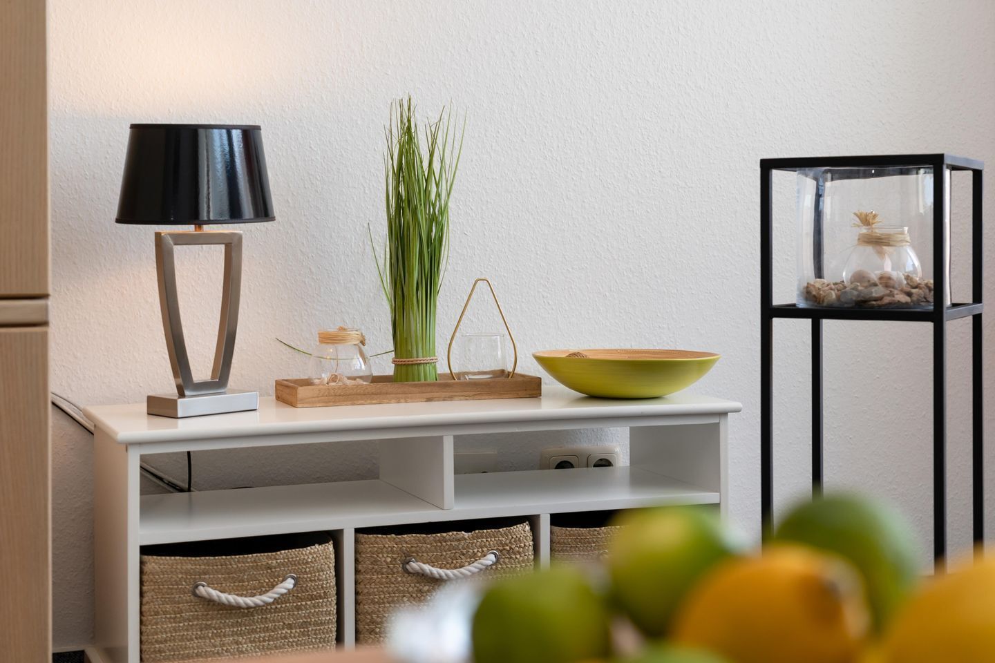 Een witte console tafel met een zwarte lamp, een groene kom, een glazen pot en een plant.
