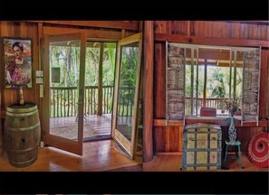 A wooden cabin with a porch, a door leading outside, and a window with a view of greenery. - 169-AUG-12-13th-AC+TreeHouse Vibe 2-BDRMS+Loft-WiFi+W&D+Ocean Cliffs. (Keaau)