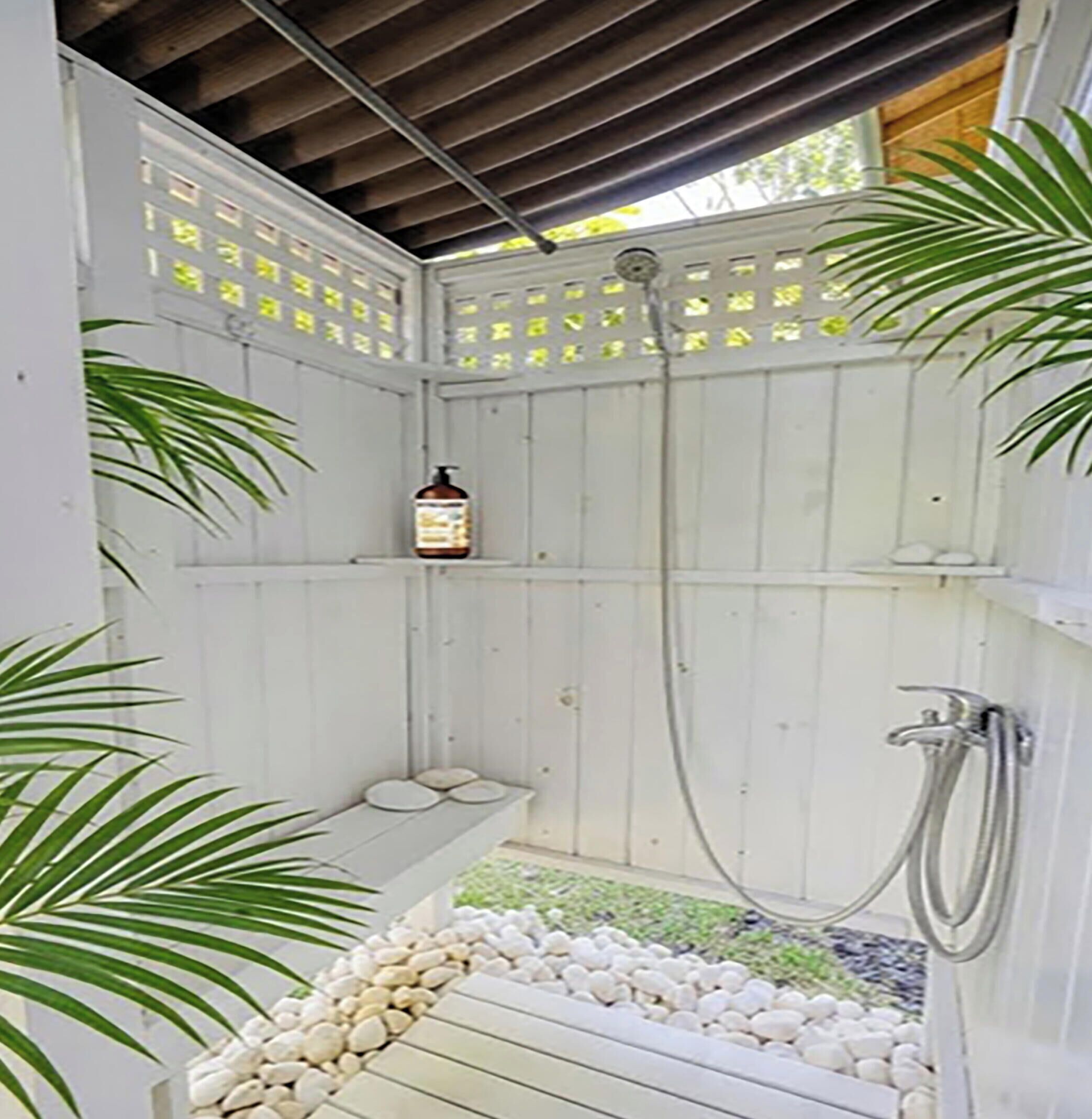 Un espace douche délimité par une clôture en bois, une étagère avec des articles de toilette et un sol recouvert de petits galets.