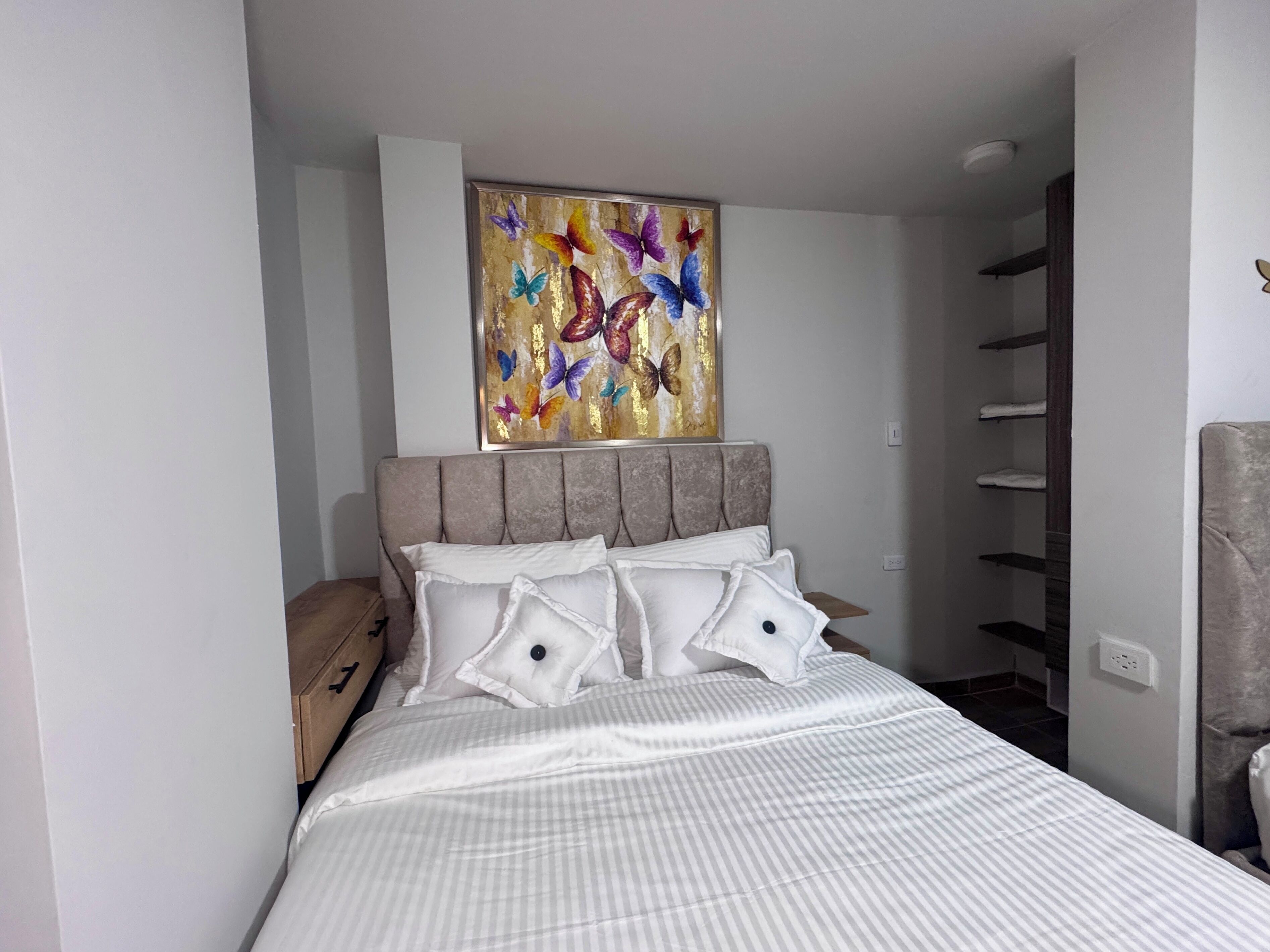 Un dormitorio con cama, almohadas, cabecera, una obra de arte en la pared y una estantería empotrada.