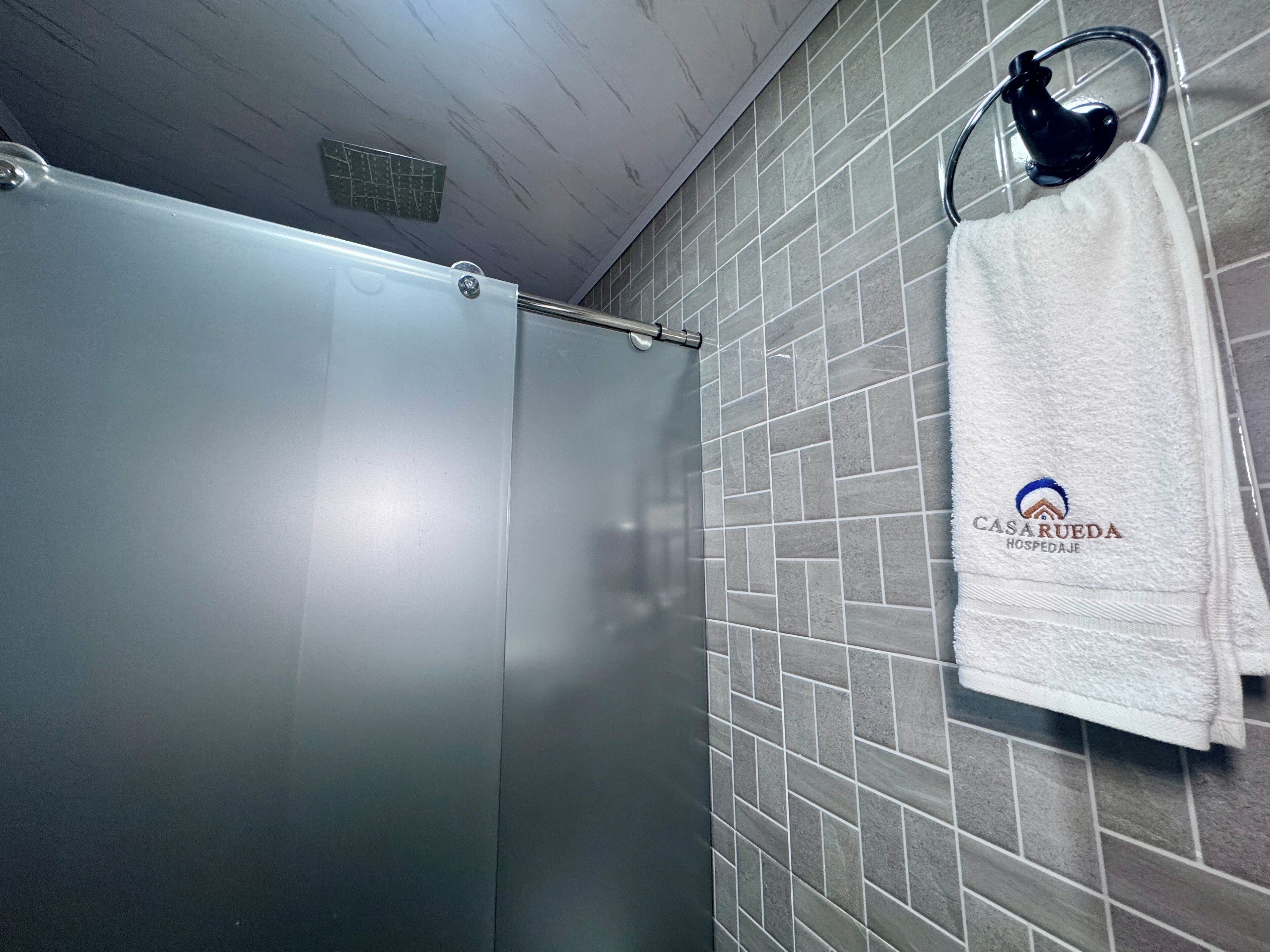 Un baño con ducha, paredes de azulejos y una toalla colgada en un perchero con un logotipo.