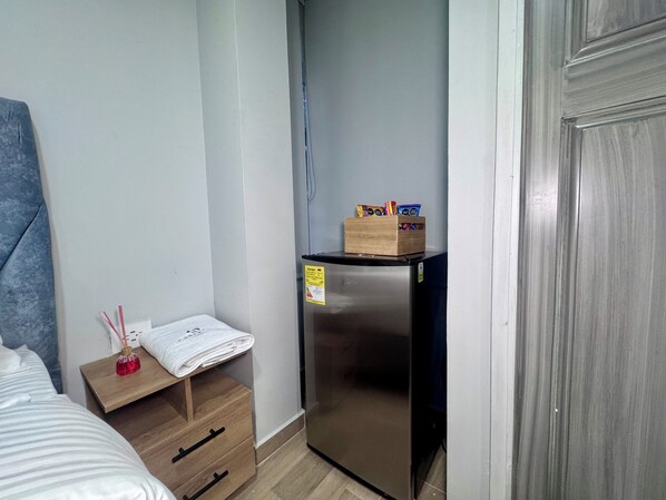A compact room with a bed, a small wooden nightstand with a tissue box and a red bottle, a built-in refrigerator, and a door to the right. - Hospedaje Casa Rueda (Barranquilla)